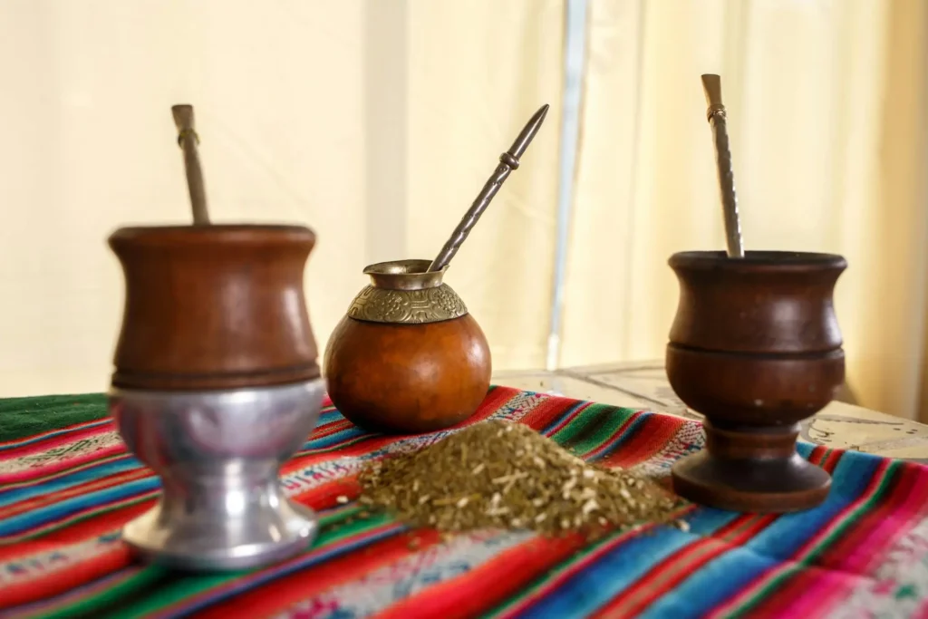Yerba mate tools hree gourd cups with bombillas placed on a colourful rag with dried yerba tea leaves in the middle.